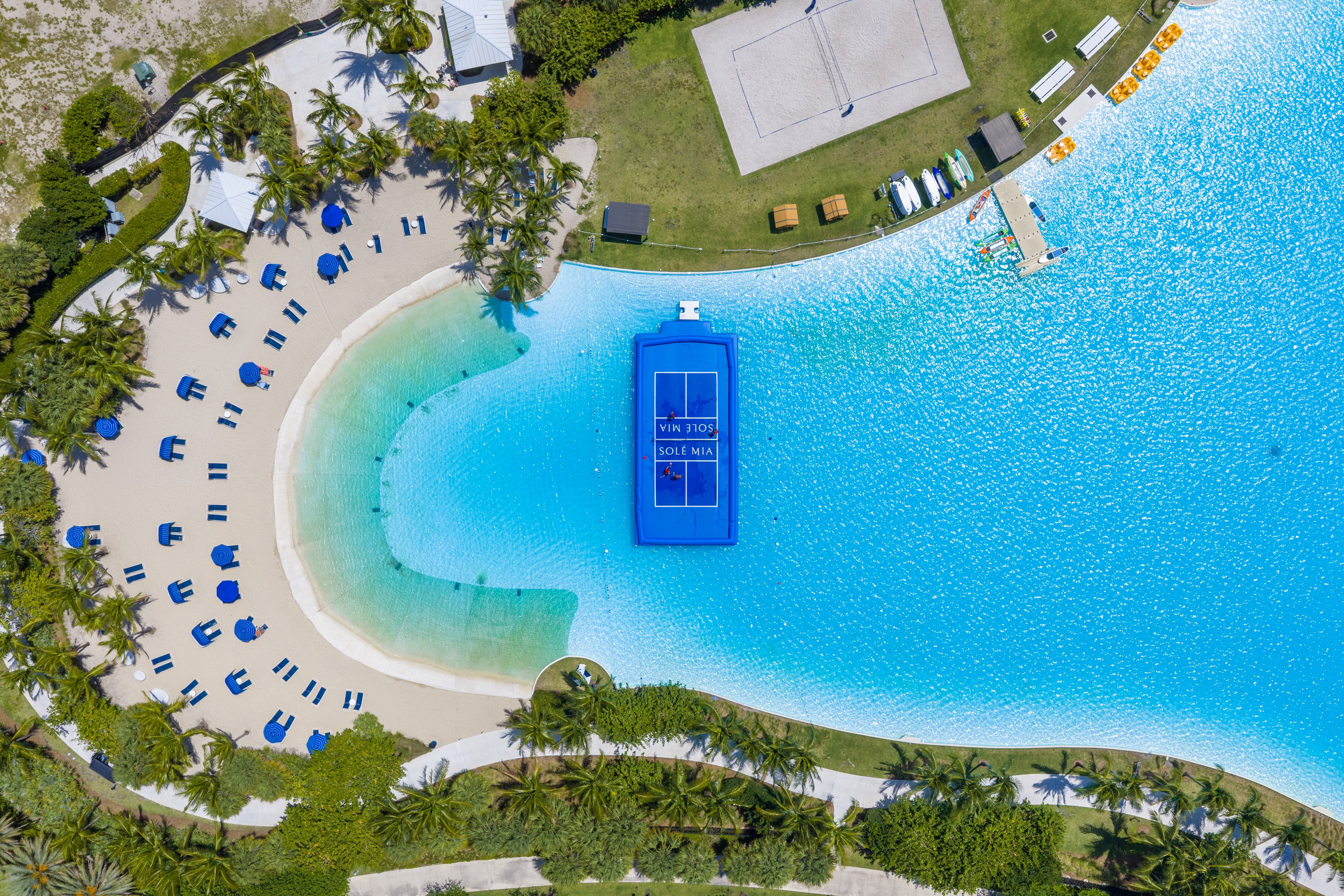 A blue swimming pool is surrounded by beach chairs and umbrellas.